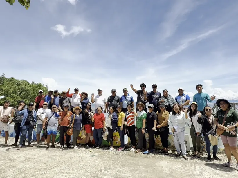 A tour group waving at a hilltop viewpoint under a blue sky
